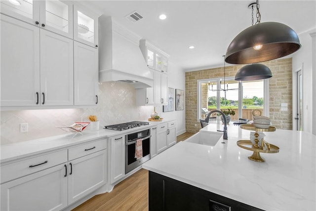 kitchen featuring hanging light fixtures, a sink, light wood-type flooring, custom range hood, and appliances with stainless steel finishes
