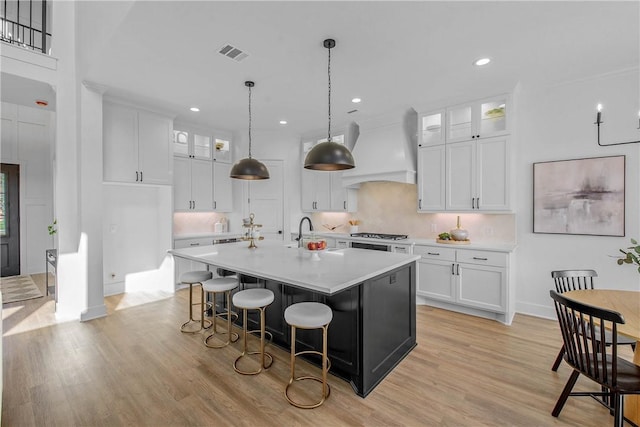 kitchen featuring light countertops, visible vents, a sink, premium range hood, and baseboards