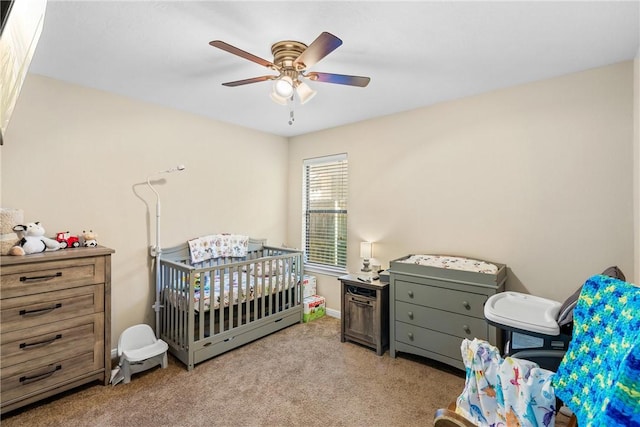 carpeted bedroom with ceiling fan and a nursery area