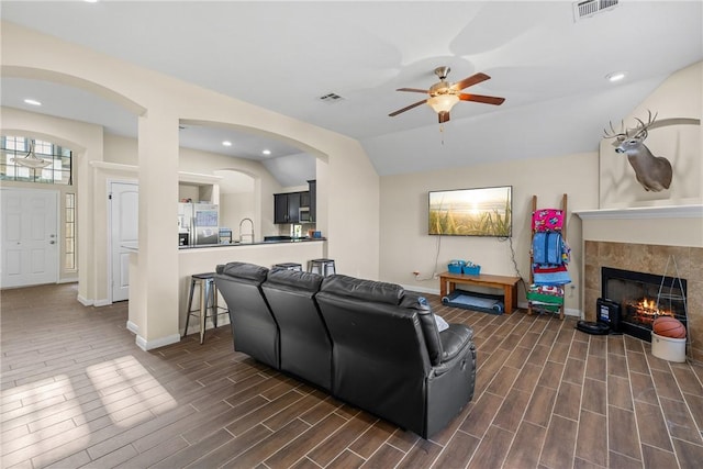 living room with sink, ceiling fan, lofted ceiling, and a tiled fireplace