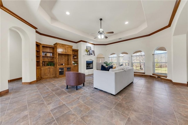 living room featuring a fireplace with raised hearth, a raised ceiling, baseboards, and ornamental molding