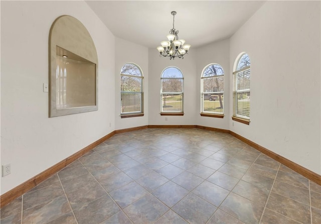 tiled spare room featuring plenty of natural light, baseboards, and an inviting chandelier