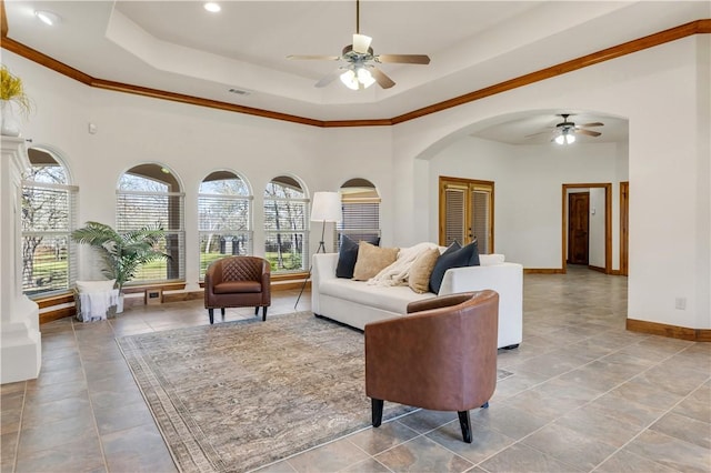 living area featuring baseboards, visible vents, a tray ceiling, arched walkways, and ceiling fan