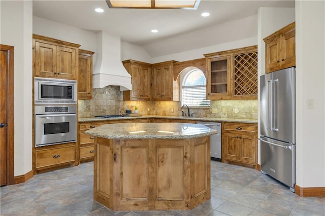 kitchen featuring a center island, light stone countertops, premium range hood, stainless steel appliances, and a sink