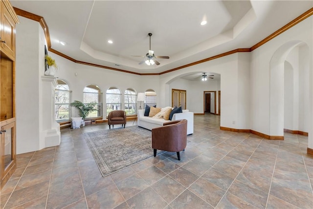 living area with a tray ceiling, crown molding, arched walkways, and baseboards