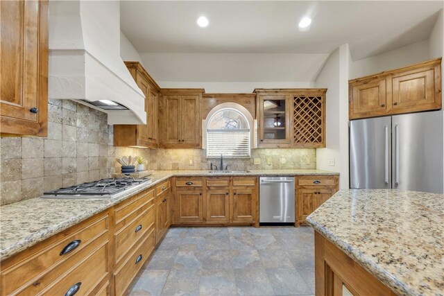 kitchen with a sink, light stone countertops, premium range hood, and stainless steel appliances