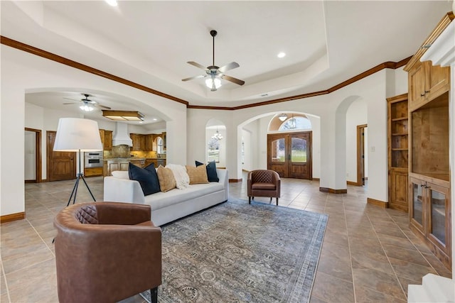 living area with tile patterned floors, baseboards, arched walkways, a raised ceiling, and a ceiling fan