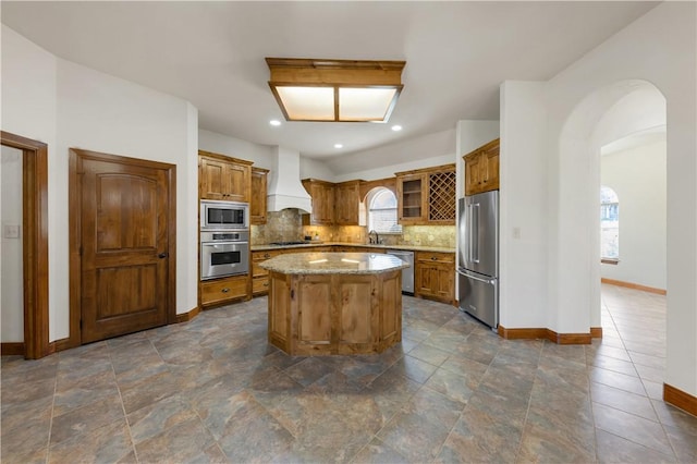 kitchen with premium range hood, decorative backsplash, arched walkways, stainless steel appliances, and a sink