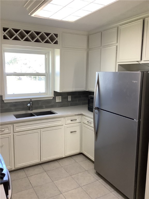 kitchen featuring light tile patterned flooring, stainless steel fridge, white cabinetry, and sink