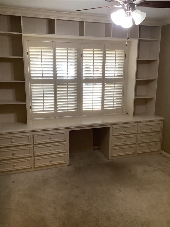 unfurnished office featuring light carpet, crown molding, ceiling fan, and built in desk