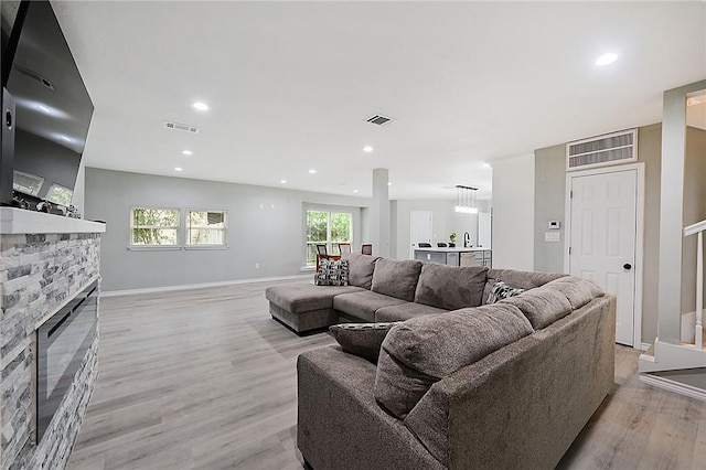 living room with a stone fireplace and light wood-type flooring