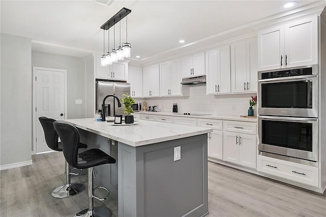 kitchen with light stone countertops, stainless steel appliances, a kitchen breakfast bar, an island with sink, and white cabinets