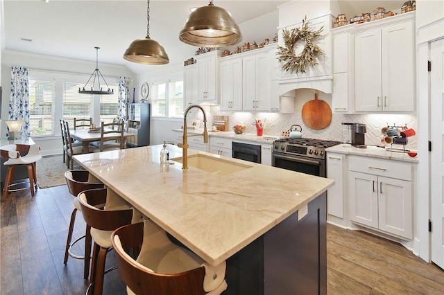 kitchen featuring gas range, decorative light fixtures, a kitchen island with sink, and white cabinets