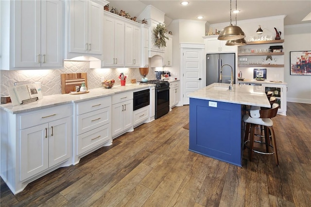 kitchen featuring pendant lighting, stainless steel fridge, white cabinets, a kitchen island with sink, and gas range oven