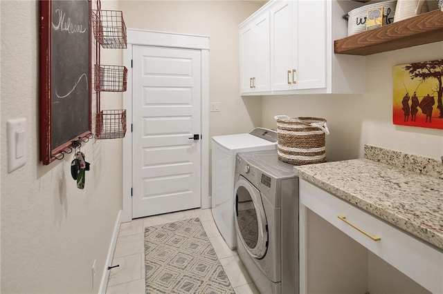 clothes washing area featuring cabinets, light tile patterned flooring, and washing machine and clothes dryer