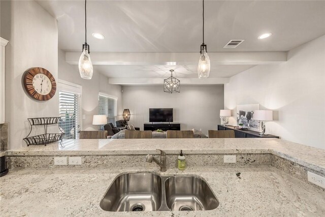 kitchen featuring light stone counters, sink, and hanging light fixtures