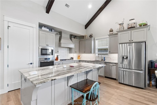 kitchen featuring light stone counters, custom range hood, stainless steel appliances, a center island, and light hardwood / wood-style floors