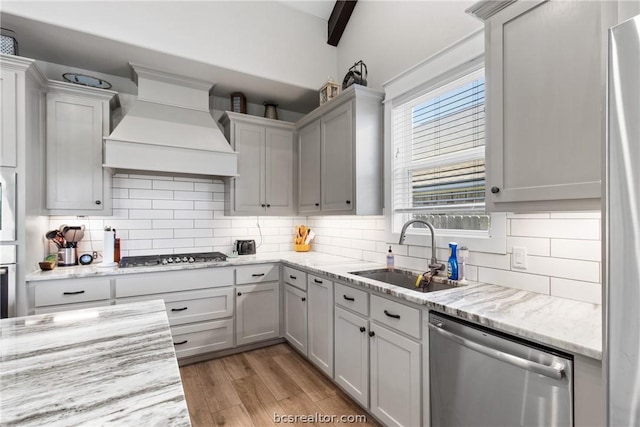 kitchen featuring sink, light hardwood / wood-style flooring, backsplash, appliances with stainless steel finishes, and custom exhaust hood