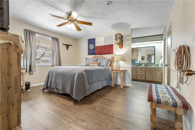 bedroom featuring ceiling fan, ensuite bathroom, light wood-type flooring, and a textured ceiling