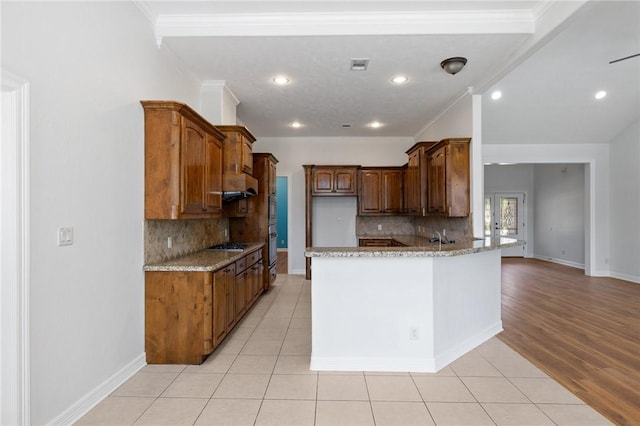4412 Hearst Ct, College Station, TX 77845 - kitchen featuring a peninsula, decorative backsplash, light stone counters, ornamental molding, and light tile patterned floors