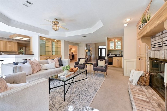 living room with a tray ceiling, ceiling fan, crown molding, and light colored carpet