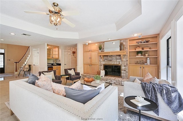 living room with a tray ceiling, a brick fireplace, ceiling fan, and crown molding