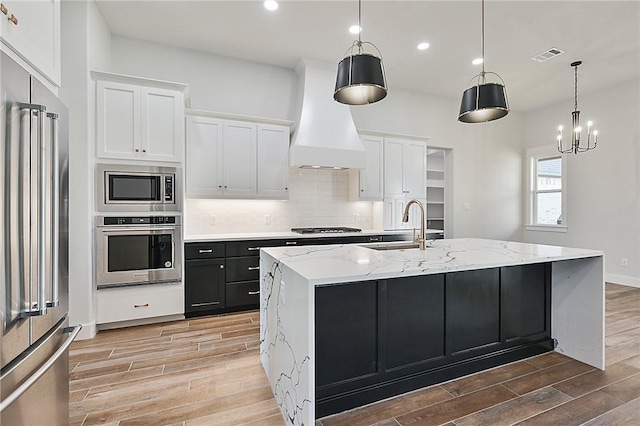 7888 Mathis Creek Dr, Bryan, TX 77808 - kitchen featuring appliances with stainless steel finishes, custom range hood, wood finish floors, white cabinets, and recessed lighting