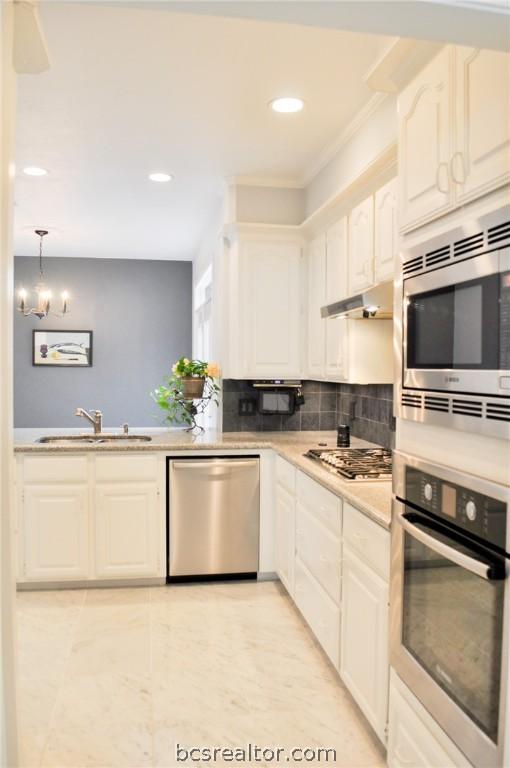 kitchen with decorative backsplash, appliances with stainless steel finishes, sink, a notable chandelier, and white cabinets