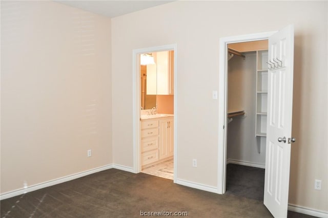 unfurnished bedroom with a walk in closet, dark carpet, ensuite bath, sink, and a closet