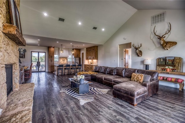 living room featuring dark hardwood / wood-style flooring, a stone fireplace, and high vaulted ceiling