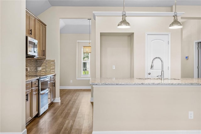 4842 Native Tree Ln, College Station, TX 77845 - kitchen with appliances with stainless steel finishes, wood finished floors, pendant lighting, backsplash, and light stone counters