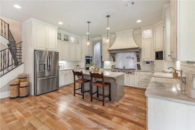 kitchen featuring white cabinetry, a center island, light wood-type flooring, appliances with stainless steel finishes, and custom exhaust hood