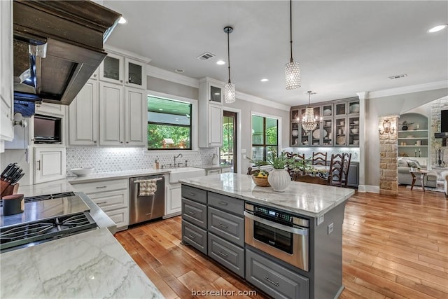 kitchen with hanging light fixtures, white cabinets, stainless steel appliances, and light wood-type flooring