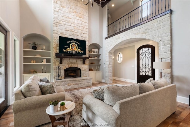 living room featuring hardwood / wood-style flooring, built in shelves, a towering ceiling, and a fireplace