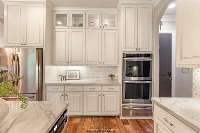 kitchen featuring white cabinets, decorative backsplash, light wood-type flooring, light stone counters, and stainless steel appliances