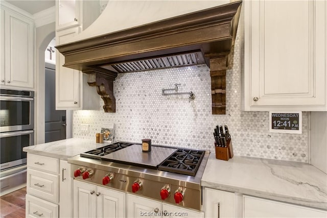 kitchen featuring stainless steel appliances, tasteful backsplash, light stone counters, custom exhaust hood, and hardwood / wood-style flooring