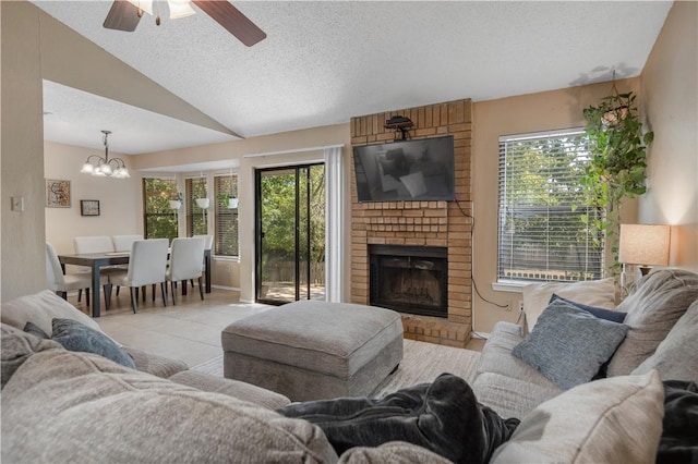 tiled living room with a fireplace, vaulted ceiling, a textured ceiling, and ceiling fan with notable chandelier