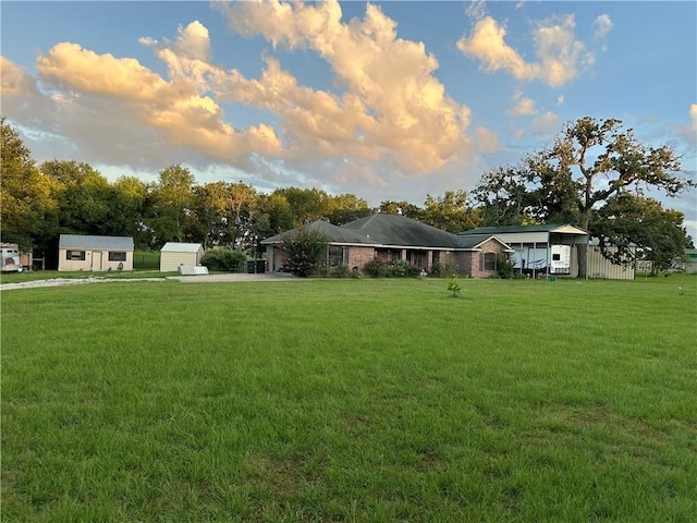 view of yard featuring an attached garage, driveway, a storage unit, and an outbuilding