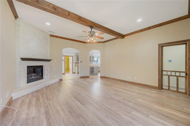 unfurnished living room with light wood-type flooring, beamed ceiling, a fireplace, and baseboards