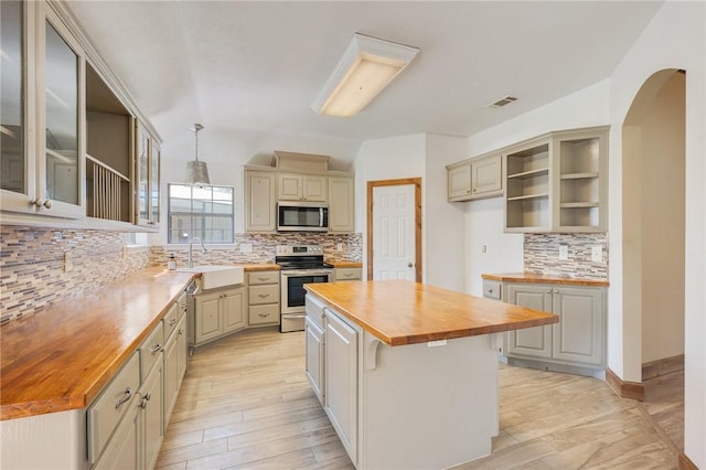 kitchen featuring a sink, a kitchen island, wooden counters, appliances with stainless steel finishes, and glass insert cabinets