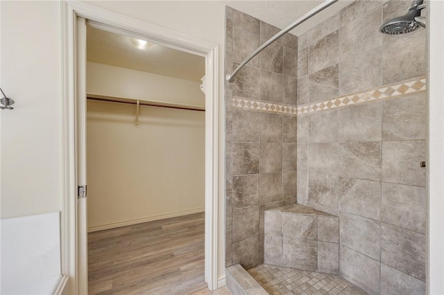 full bathroom with wood finished floors, a walk in closet, and a shower stall