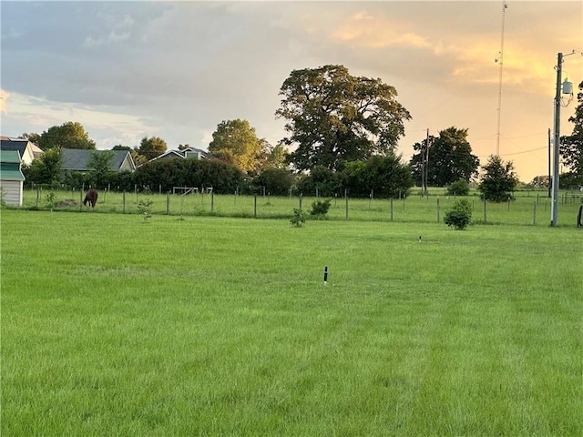 yard at dusk featuring a rural view and fence