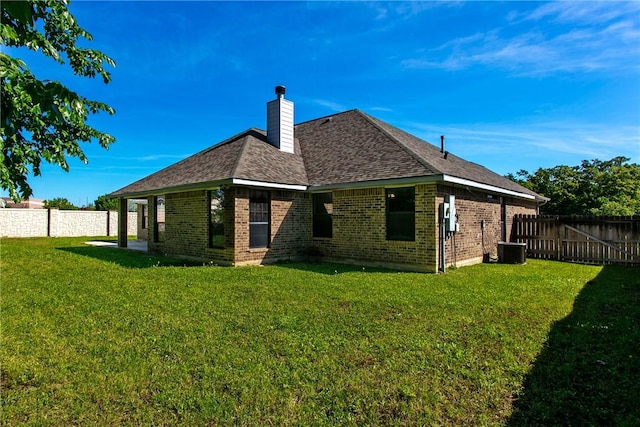 back of house with brick siding, a fenced backyard, a lawn, and a chimney