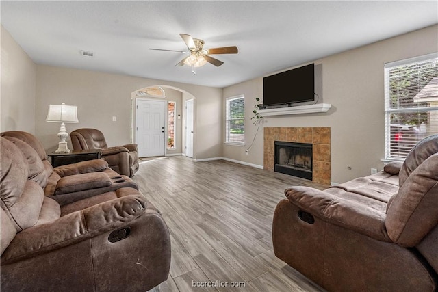 living room with a tiled fireplace, a wealth of natural light, light hardwood / wood-style floors, and ceiling fan