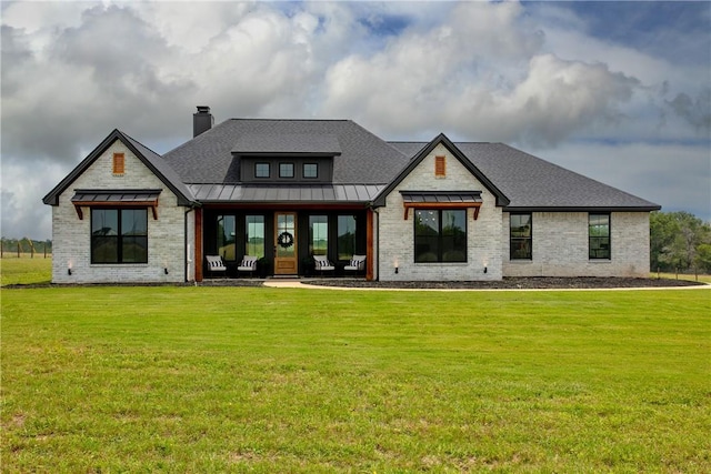 rear view of house featuring brick siding, a lawn, a chimney, metal roof, and a standing seam roof