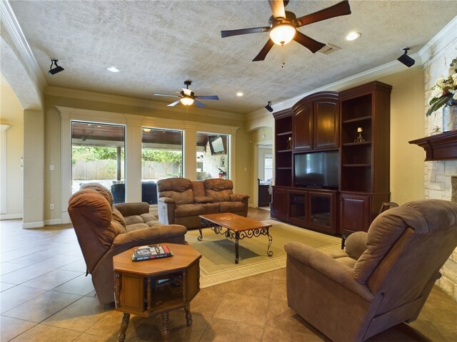 tiled living room featuring ceiling fan, a stone fireplace, crown molding, and french doors