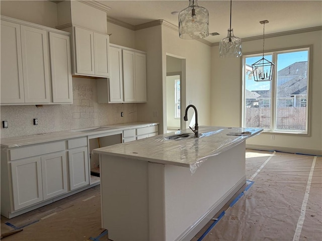 kitchen featuring white cabinetry, hanging light fixtures, light stone counters, tasteful backsplash, and a center island with sink