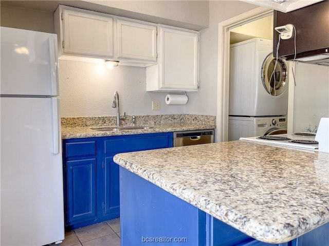 kitchen with blue cabinetry, white cabinetry, white fridge, and stacked washing maching and dryer