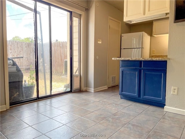 interior space featuring white fridge, light stone counters, blue cabinets, and light tile patterned floors