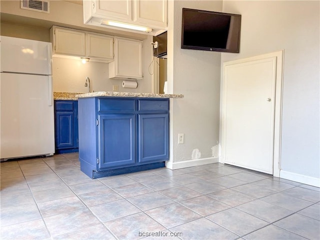 kitchen featuring sink, light tile patterned floors, blue cabinetry, white fridge, and light stone counters